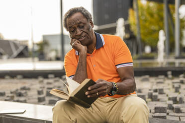 Älterer Mann mit Hand am Kinn, der ein Buch liest - JCCMF08215