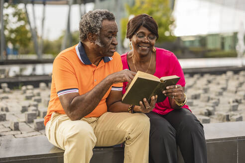 Älteres Paar, das an der Wand sitzend ein Buch liest - JCCMF08216