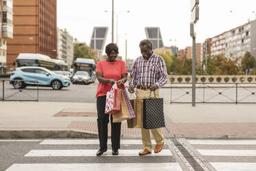 Glückliches Paar mit Einkaufstüten beim Überqueren der Straße in der Stadt - JCCMF08227