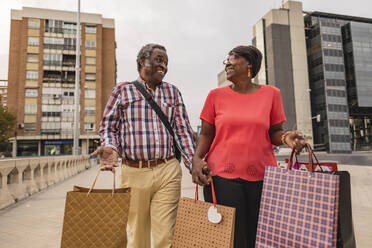 Glückliches älteres Paar, das mit Einkaufstüten auf dem Fußweg geht - JCCMF08255