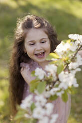 Happy cute girl plucking cherry blossom flowers in garden - ONAF00271