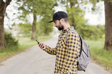 Mann mit Mütze benutzt Smartphone auf der Straße - ONAF00273