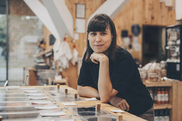 Smiling store owner leaning on counter in zero waste shop - NDEF00143