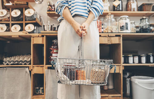 Customer holding jars filled with lentils in shopping basket at shop - NDEF00158