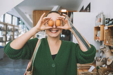 Smiling customer covering eyes with eggs in shop - NDEF00174