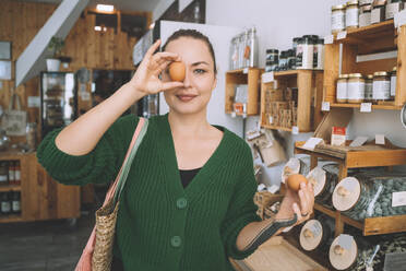 Woman covering eye with egg in zero waste store - NDEF00175