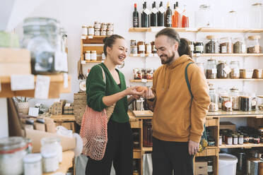 Smiling man and woman holding eggs in zero waste shop - NDEF00178