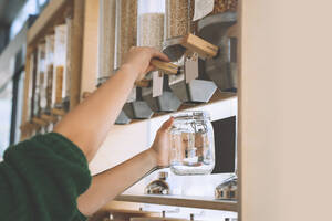 Customer filling lentils in glass jar at zero waste shop - NDEF00185