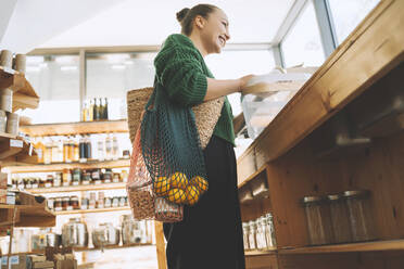 Smiling woman with fruits and groceries in mesh bags at store - NDEF00203