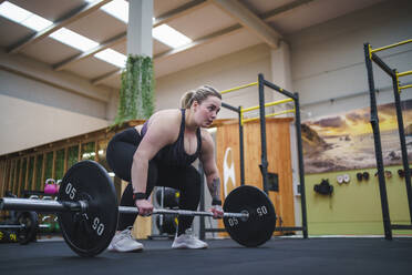 Confident overweight woman exercising with barbell in gym - SNF01608