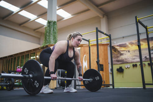 Selbstbewusste übergewichtige Frau, die mit einer Langhantel im Fitnessstudio trainiert - SNF01608