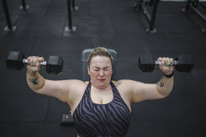 Engagierte übergewichtige Frau bei einer Übung mit Hanteln im Fitnessstudio - SNF01610
