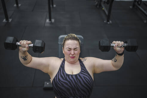Dedicated overweight woman doing exercise with dumbbells in gym - SNF01610