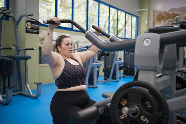 Übergewichtige Frau bei einer Schulterübung im Fitnessstudio - SNF01619