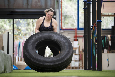 Entschlossene junge Frau, die in einem Fitnessstudio mit Reifen trainiert - SNF01621