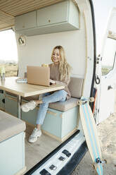 Glücklicher digitaler Nomade arbeitet am Laptop im Wohnmobil - RCPF01503