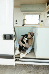 Happy woman embracing dog sitting in camper van - RCPF01506