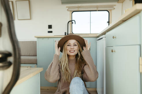 Glückliche junge Frau mit Hut im Wohnmobil sitzend - RCPF01521