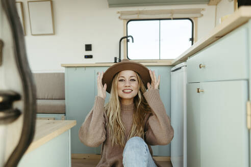 Happy young woman wearing hat sitting inside motor home - RCPF01521