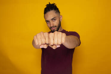 Confident man showing fists against yellow background - DSIF00627