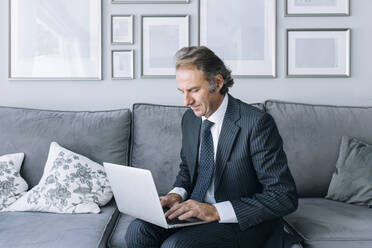 Geschäftsmann mit Laptop auf dem Sofa sitzend bei der Arbeit zu Hause - EGHF00651