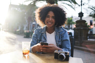 Lächelnde Frau mit Smartphone, die in einem Straßencafé sitzt - ASGF03100