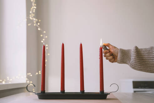 Frau verbrennt rote Adventskerze mit Feuerzeug zu Hause - NDEF00212