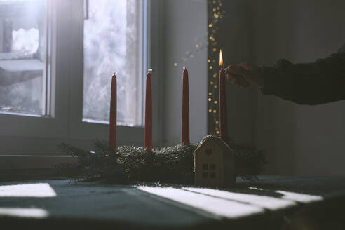 Frau brennt Kerze auf Tannenkranz zu Hause in Weihnachten - NDEF00213