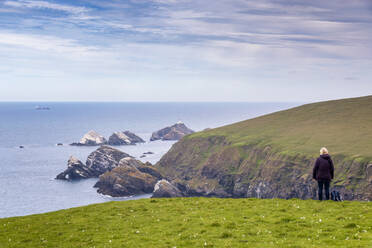 UK, Schottland, Unst, Wanderin steht auf einer Klippe und blickt auf den Muckle Flugga Leuchtturm - SMAF02466