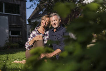 Lächelndes reifes Paar sitzt auf Gras im Hinterhof - JOSEF14847
