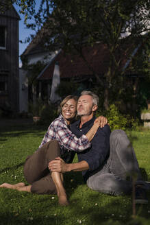 Lächelnde reife Frau umarmt Mann auf Gras sitzend - JOSEF14850