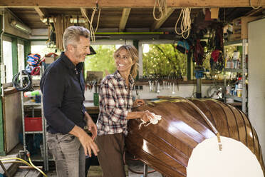 Glücklicher Mann mit Frau beim Polieren eines Bootes in der Garage - JOSEF14864