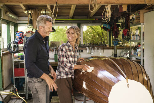 Happy man with woman polishing boat in garage - JOSEF14864