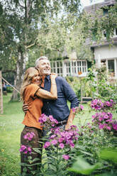 Happy woman hugging man standing by flowering plants - JOSEF14879