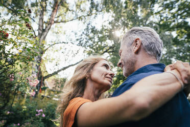 Smiling mature woman hugging man under tree on sunny day - JOSEF14981