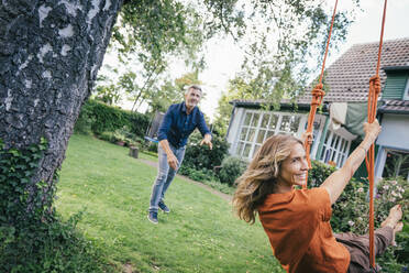 Mature man with woman enjoying on swing in back yard - JOSEF14997