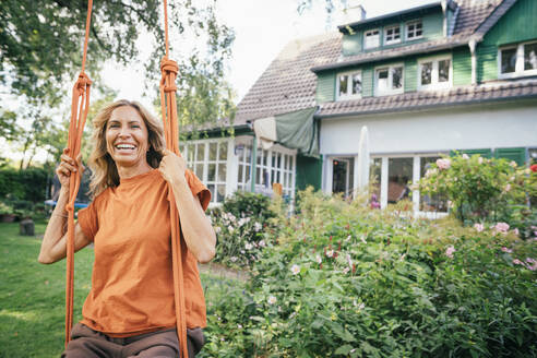 Fröhliche reife Frau sitzt auf einer Schaukel vor einem Haus - JOSEF15002