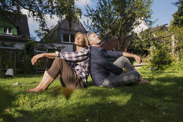Älterer Mann und Frau mit geschlossenen Augen sitzen auf Gras im Hinterhof - JOSEF15008
