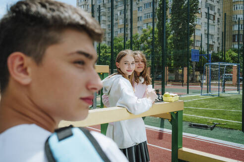 Teenage girls looking at boy in schoolyard - MDOF00249