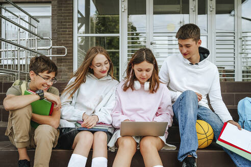 Pupils doing homework using laptop sitting on steps - MDOF00254