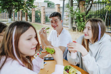 Glückliche Freunde beim Mittagessen am Tisch auf dem Schulhof - MDOF00258