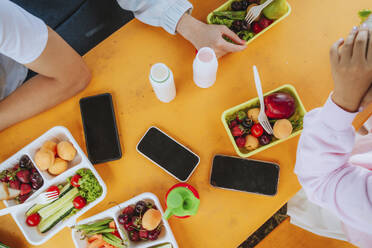 Teenage pupils having lunch sitting at table with smart phones - MDOF00262