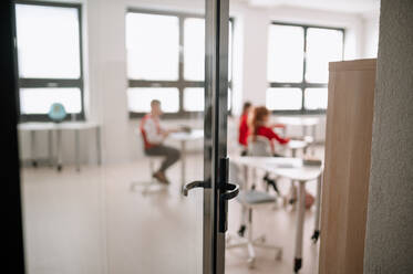 Blick von hinten durch die offene Tür in die Klasse auf die Schüler, die im Klassenzimmer sitzen und dem Lehrer zuhören - HPIF00005