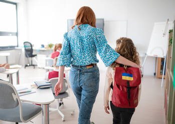 Rückansicht eines Lehrers mit einer ukrainischen Schülerin im Klassenzimmer, Konzept der Einschulung ukrainischer Kinder in Schulen. - HPIF00007