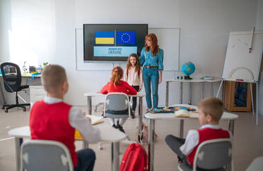 A teacher welcoming Ukrainian schoolgirl in classroom, concept of enrolling Ukrainian kids to schools. - HPIF00008