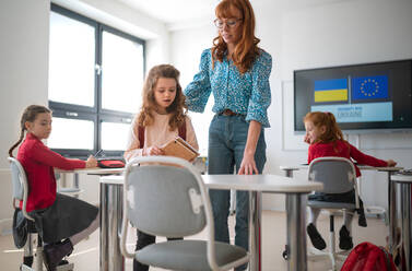 A teacher with Ukrainian schoolgirl in classroom, concept of enrolling Ukrainian kids to schools. - HPIF00009