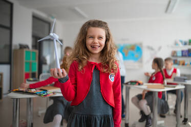 A schoolgirl holding wind turbine and learning about eco-friendly renewable sources of energy in classroom at school - HPIF00022