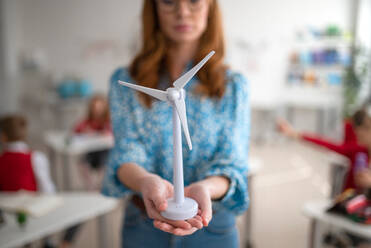 Nahaufnahme eines Grundschullehrers, der ein Modell einer Windturbine hält und Kinder über umweltfreundliche Formen erneuerbarer Energie unterrichtet - HPIF00026