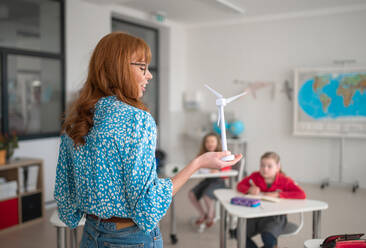 An elementary school teacher holding model of wind turbine and learning kids about eco-friendly forms of renewable energy - HPIF00027