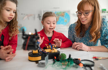 Eine Gruppe von Kindern mit einem jungen Lehrer für Naturwissenschaften programmiert elektrische Spielzeuge und Roboter im Robotik-Klassenzimmer - HPIF00033